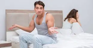 A couple sitting on a bed in a bedroom, discussing erectile dysfunction and premature ejaculation.