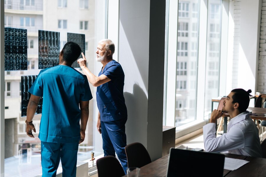 back-view-team-multiethnic-doctors-discussing-together-history-disease-patient-using-mri-scan-medical-conference-standing-near-window