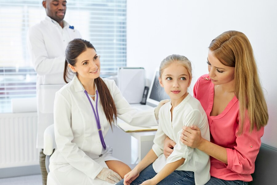 Doctor talking to child and his mother during health checkup at the clinic, mom and girl get consultation by professional pediatrician or general practitioner during visit to the hospital